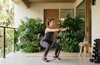 Woman in her 30s doing resistance band squat row on tropical outdoor porch