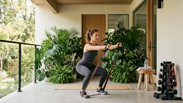 Woman in her 30s doing resistance band squat row on tropical outdoor porch