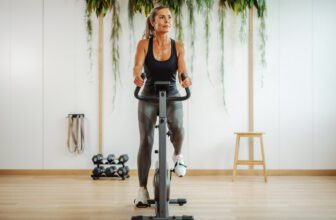 A fit woman in her 40s using stationary bike for her workout in a home gym.