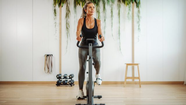A fit woman in her 40s using stationary bike for her workout in a home gym.